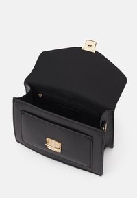 Czarna skórzana torebka na ramię z złotym zapięciem, wyposażona w przednią kieszeń i wewnętrzną kieszeń na zamek, o gładkiej fakturze i starannej konstrukcji.