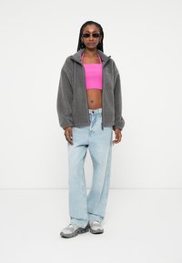 Giacca in pile con zip grigia, top cropped rosa, jeans a gamba larga blu chiaro e sneakers grigie. Presenta una vestibilità comoda e hardware minimale.