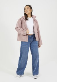 Veste imperméable rose clair avec une fermeture éclair à l'avant, des manches larges et un col haut, assortie à un pantalon en denim bleu ample et des baskets blanches.
