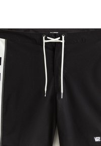 Sorte svømshorts med en hvid snor, sidelommer og et Vans-logo. Materialet ser glat og let ud.