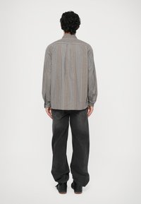 Camicia a maniche lunghe grigia a righe con vestibilità rilassata, abbinata a jeans scuri larghi e scarpe nere. La camicia presenta un colletto con bottoni.