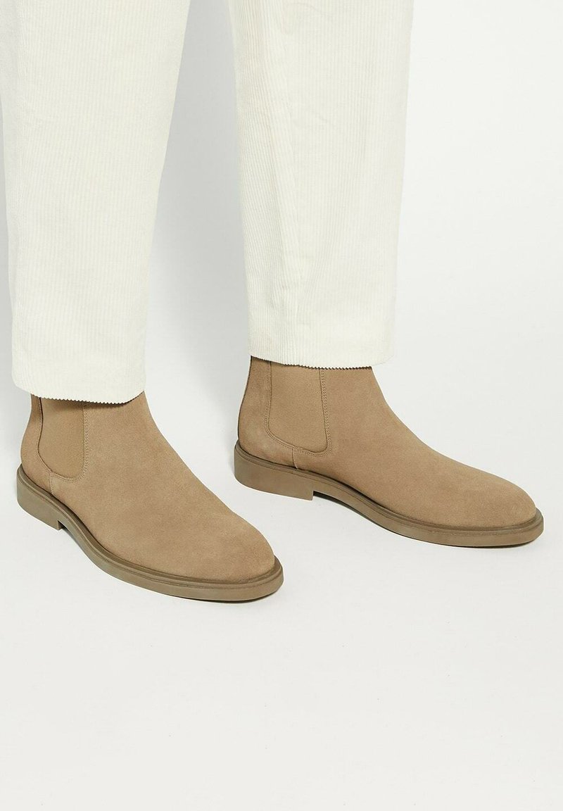 Tan suede ankle boots with elastic side panels and a smooth, rounded toe. Features a flat rubber sole and minimal stitching accents.