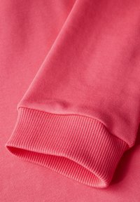 Tejido de sudadera rosa con puños acanalados. La textura es suave con detalles de tejido fino, enfatizando un ajuste relajado y una sensación de suavidad.