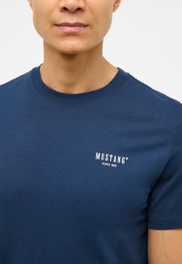 Tengerészkék kerek nyakú póló, pamutból készült, bal mellrészen található egy kis fehér "MUSTANG" logó és a "SINCE 1932" felirat.