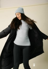 Fekete puffdzseki, világosszürke bordás pulóver és fekete leggings; laza öltözet, változatos textúrákkal és testhezálló dizájnnal. Világosszürke sapka.