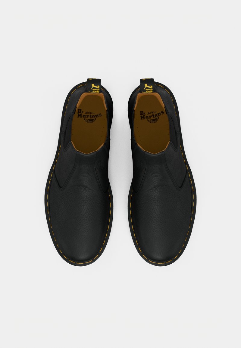 Pair of black leather slip-on Dr. Martens shoes with yellow stitching and branded pull tabs, viewed from above on white background.