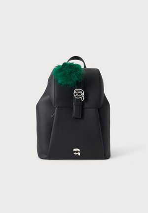 Sort tekstureret rygsæk med klap og strop, dekoreret med grøn fluffy pompom og to små sølvfarvede metal accenter i form af ansigter.