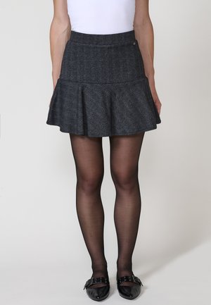 Jupe évasée en chevron gris avec une taille cintrée, tissu texturé et un accent de bouton décoratif. Assortie avec des collants noirs transparents et des ballerines.