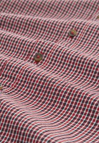 Rot- und blaumusterstoff mit einem kleinen Rautenmuster, verziert mit braunen Knöpfen an der Knopfleiste, zeigt eine glatte und strukturierte Oberfläche.