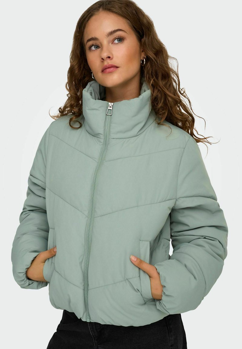Polstret jakke i lys grøn med høj krave, lynlås lukning og to sidelommer. Har vandret syning for tekstur.