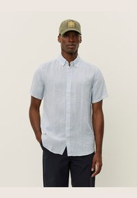 Lyseblå kortermet skjorte med hvite vertikale striper, knappekrage og slim-fit. Laget av bomull, kombinert med en olivengrønn caps.