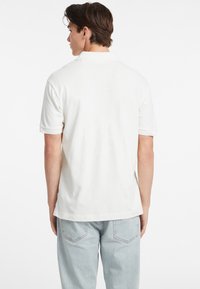 Polo shirt in cotone bianco con maniche corte, colletto classico e orlo dritto, abbinato a jeans azzurri a vita bassa e taglio rilassato.