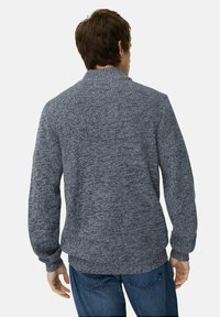 Donkerblauwe gebreide trui met een hoge kraag, lange mouwen en een aansluitende taille. Heeft een gebreid patroon en geribbelde boorden.