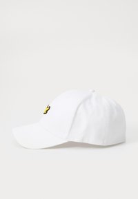 Casquette de baseball blanche en coton. Elle possède un visière incurvée, une sangle ajustable et un petit logo de papillon jaune à l'avant.