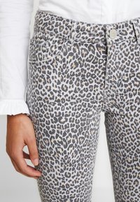 Jeans de denim con estampado de leopardo sobre una base gris, con un diseño ajustado, bolsillos frontales y un cierre de botón metálico en la cintura.