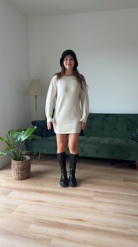 Vestido de malha cremosa com mangas bufantes, combinado com botas pretas até ao joelho. Em frente a um sofá verde e um chão de madeira.