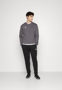 Grå langærmet sweatshirt og sorte sweatpants med Adidas-logoer, båret med en hvid skjorte underneath og sorte træningssko.