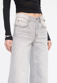 Jeans de tiro alto en gris claro con un corte relajado, diseño de cinco bolsillos y un desgaste sutil. Hechos de denim con una textura suave.