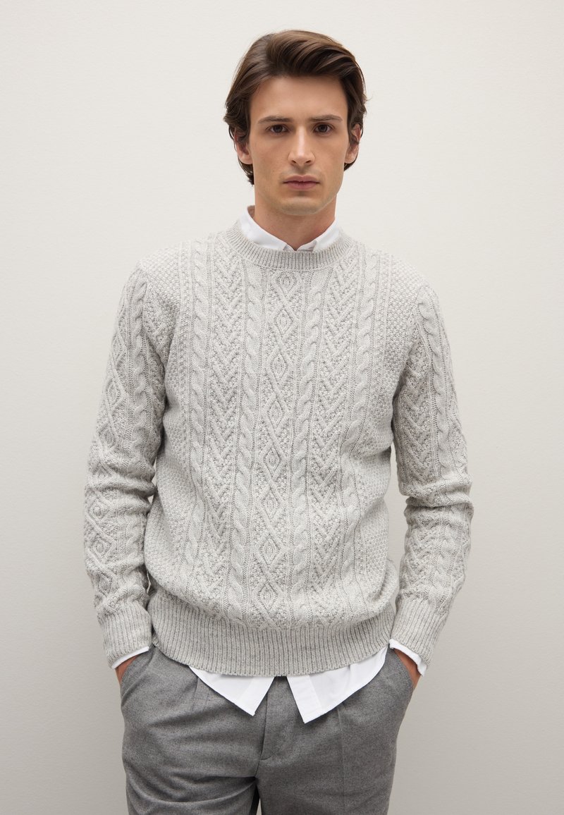 Grauer gestrickter Pullover mit einem strukturierten Zopfmuster, ausgestattet mit einem Rundhalsausschnitt und gerippten Bündchen, über einem weißen Hemd mit Kragen getragen.