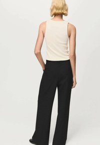 Top sin mangas color crema y pantalones de pierna ancha negros. La parte superior es ajustada con una textura acanalada, mientras que los pantalones tienen un acabado suave y una cintura alta.