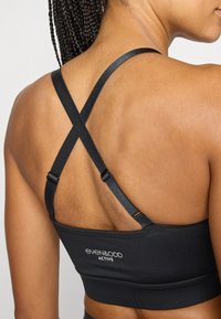 Svart sports-BH med teksturert, elastisk stoff, racerback-design, justerbare stropper og subtil merkevare på båndet.