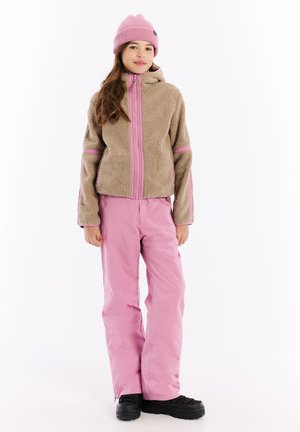 Beige fleece jack met roze accenten, ritssluiting aan de voorkant en capuchon. Lichtroze sneeuwbroek, zwarte laarzen. Model staat tegen een witte achtergrond.