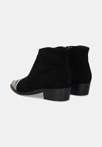 Botines de ante negro con un tacón grueso, que presentan un patrón a rayas en la punta. Cierre de cremallera en la parte trasera. Textura suave.