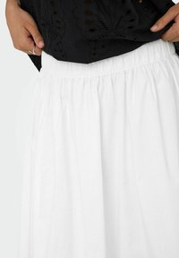 Vit kjol med elastisk midja och en flödande design och mjuk textur, med samlad tyg för volym och en slät, minimalistisk look.