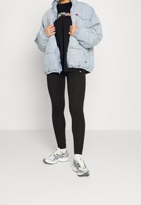 Jasnoniebieska kurtka puchowa, czarny t-shirt z kolorowym napisem, czarne leginsy i srebrne buty sportowe z niebieskimi akcentami.