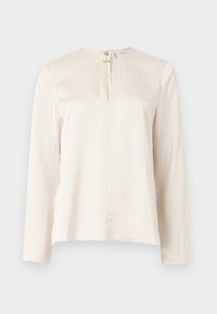 Blouse à manches longues couleur écrue avec un col rond et une fermeture éclair centrale. Texture lisse, design minimaliste, et coupe légèrement carrée.