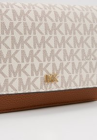 Portefeuille beige et marron Michael Kors avec motif répétitif du logo MK et emblème doré MK sur surface texturée.