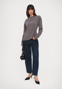 Maglia grigia a maniche lunghe con tessuto strutturato, taglio dritto e dettagli sulle cuciture laterali, abbinata a jeans in denim scuro e tacchi a punta neri.