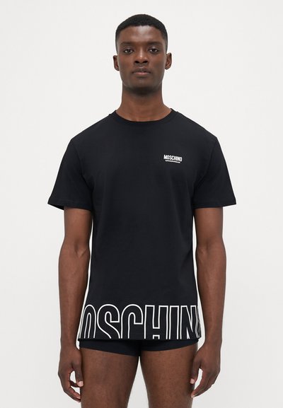 T-shirt in cotone nero con collo tondo, maniche corte e un audace logo bianco "MOSCHINO" lungo il fondo. Design semplice, tessuto morbido.