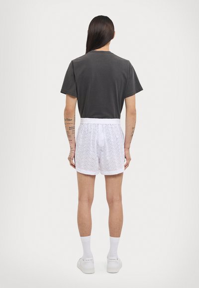 Gray cotton t-shirt paired with white eyelet shorts. The shorts feature a textured pattern and elastic waistband, with white socks and sneakers.