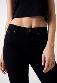 Jeans in denim nero con design aderente, caratterizzati da cinque tasche, chiusura frontale con bottoni e dettagli di cuciture sottili.