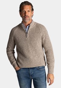 Beige gebreide trui met een halve rits en een neklap, met geribbelde textuur, gecombineerd met klassieke blauwe jeans in een casual pasvorm.