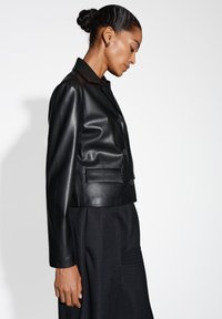 Zwarte cropped leren jas met een gladde textuur, knoopsluiting aan de voorkant en twee voorzakken. Gemaakt met lange mouwen en een gekarteld kraag.