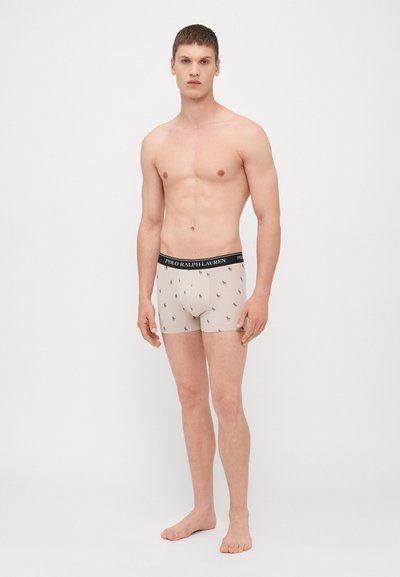 Beige boxershorts met een zwarte elastische tailleband waarop het logo "Polo Ralph Lauren" staat; versierd met kleine donkere patroondetails overal.