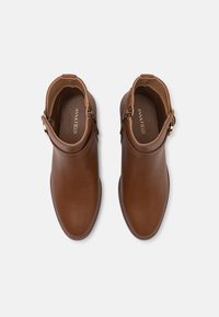 Bottines en cuir marron avec une texture lisse, bout arrondi, fermeture éclair et une sangle accent avec une boucle en ton doré.