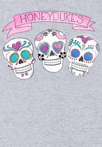 Tři barevn�é cukrové lebky se srdcovitýma očima pod růžovým transparentem s nápisem "HONEYDUKES" na světle šedém pozadí.