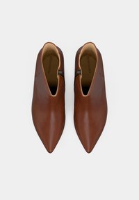 Pari ruskeista nahkaisista nilkkakengistä, joissa on terävä kärki ja sivuvetoketju, esitelty ylhäältä päin valkoista taustaa vasten.