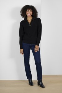 Pull noir à côtes avec col zippé, assorti à un pantalon en jean bleu foncé et des bottines noires. L'ensemble présente un design épuré et moderne.