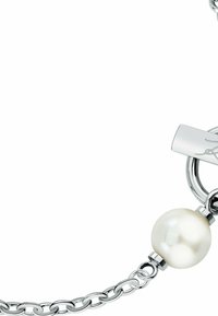 Silberarmband mit Kette, das eine große weiße Perle zeigt, die an einem runden Glied mit flachem Verschluss befestigt ist, auf dem ein Logo eingraviert ist.