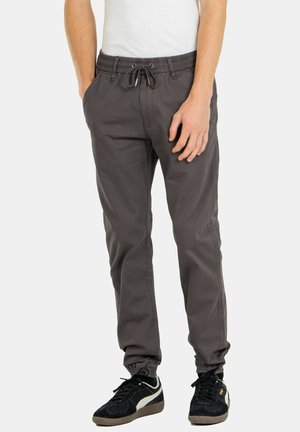 Pantalones jogger grises con cintura elástica, cordón y puños elásticos. La tela es suave, con bolsillos laterales y un ajuste relajado.
