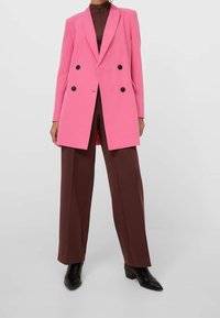 Rosa zweireihiger Blazer mit schwarzen Knöpfen, maßgeschneidertem Design, Revers mit Kerbe, kombiniert mit brauner Hose mit weitem Bein und schwarzen Stiefeletten.