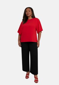 Top rosso a maniche corte abbinato a pantaloni neri a gamba larga e sandali rossi con cinturini. Il top presenta una vestibilità comoda e una texture liscia.
