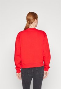 Czerwona bluza z okrągłym dekoltem, ściągaczami przy mankietach i luźnym krojem, zestawiona z ciemnoszarymi jeansami. Gładka faktura, bez wzorów i zdobień.
