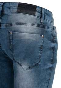 Blaue Jeans aus Denim mit einer verblassten Optik, ausgestattet mit einem schwarzen Lederpatch am Bund, Metallnägeln und einer Gesäßtasche mit einer geschwungenen Gestaltung.