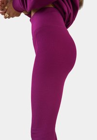 Fitted leggings in een opvallende roze kleur, met ribbeltextuur, hoge tailleband, en een gladde afwerking die de vorm van de benen benadrukt. Geen versieringen of patronen.
