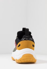 Baskets Calvin Klein Jeans avec une tige en maille noire, des accents gris et rouge, un talon en daim jaune et une semelle intermédiaire blanche ; semelle en caoutchouc texturée.